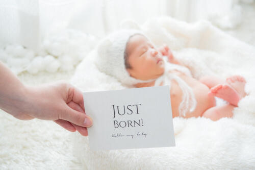 「JUST BORN」と書かれたおしゃれなカードと白い帽子をかぶった赤子のニューボーンフォト（撮影：mica*camera　田中美香）