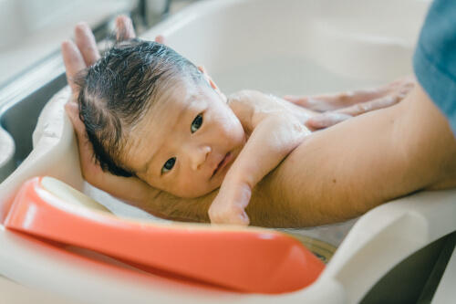 パパの腕に支えられながら沐浴する小さな赤ちゃんの新生児写真（撮影：モロズミケイタ）