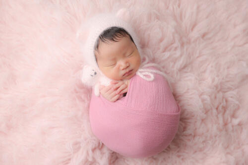 ピンクのおくるみに包まれて胎内音を聞きながら眠る新生児の赤ちゃんの写真（撮影：fluffy babysおおさわ）