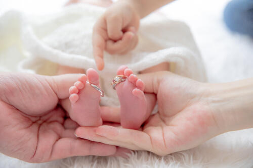 結婚指輪をかけた新生児の足と、お母さんとお父さんと2歳の子供の手と一緒に撮影したニューボーンフォト（撮影：山﨑早江子）