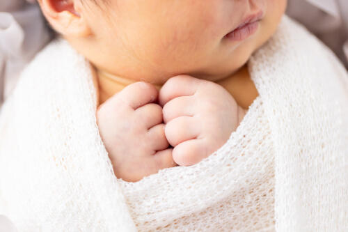 おくるみに巻かれて安心している赤ちゃんのかわいい手を写したニューボーンフォト（撮影：つちやまい）