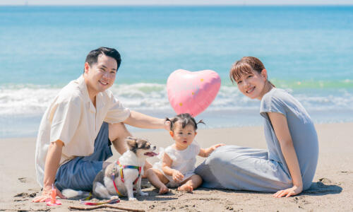 爽やかな青い海とピンクの風船を背景に、ママ・パパ・女の子・ペットの犬で撮影した家族写真（撮影：リーナ）