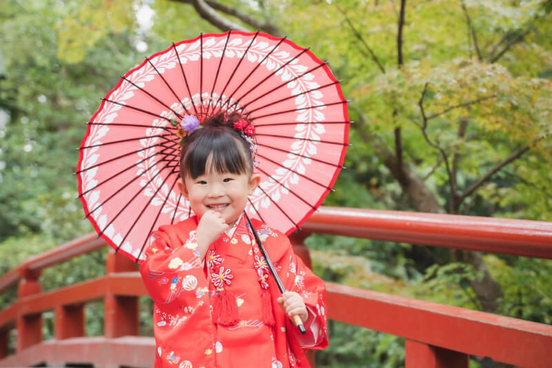 赤い和傘と着物を身につけて桟橋の上に立つ、七五三の女の子の写真（撮影：LaLagenic Photo）