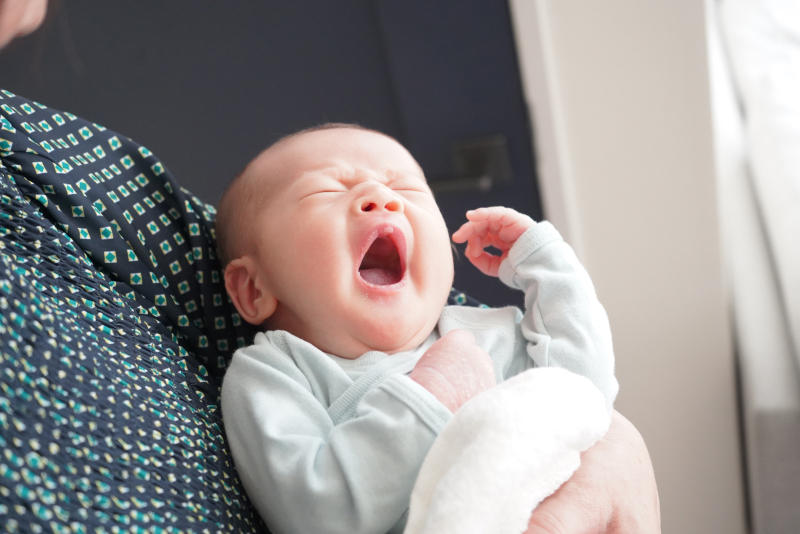 抱っこされながら大きくあくびをする新生児