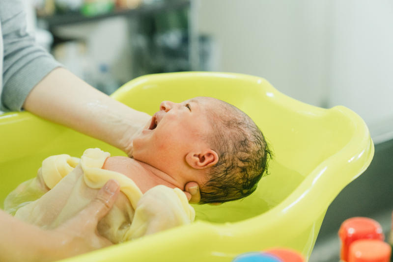 黄色いベビーバスの中で口を開け笑顔を見せながら沐浴をする新生児