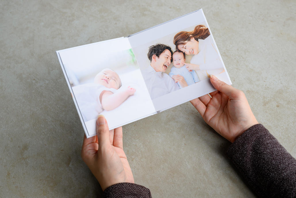 白い服を着た眠る乳児の写真と笑顔の家族写真のフォトブックを持つ手元の写真