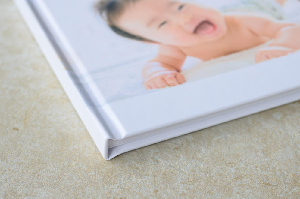 うつ伏せで顔を上げて笑う乳児の写真が表紙になったフォトブックの背の一部を写した写真